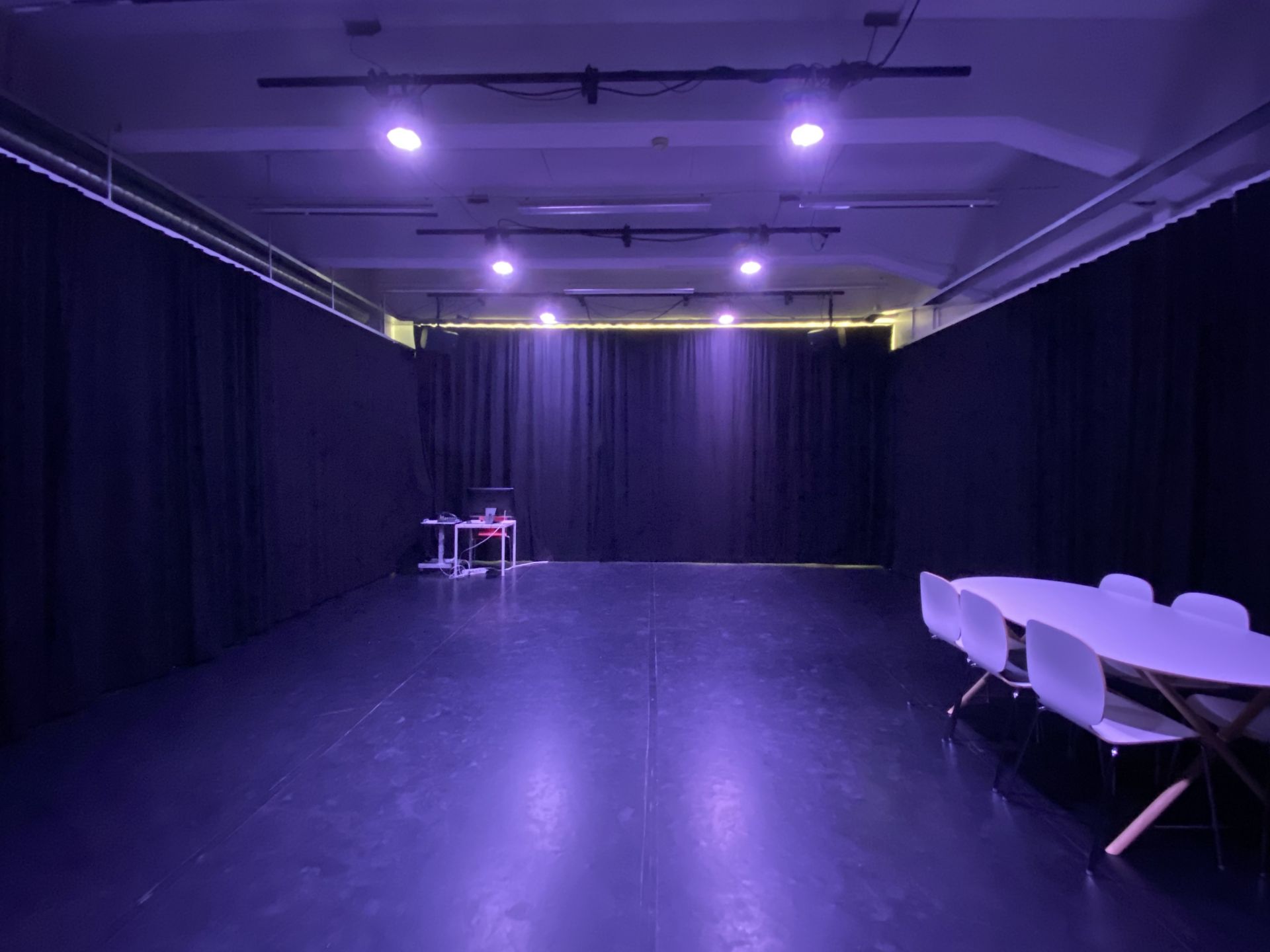 En studio med svart matta och svarta gardiner längs väggarna. I taket lyser lampor med ett blått sken.