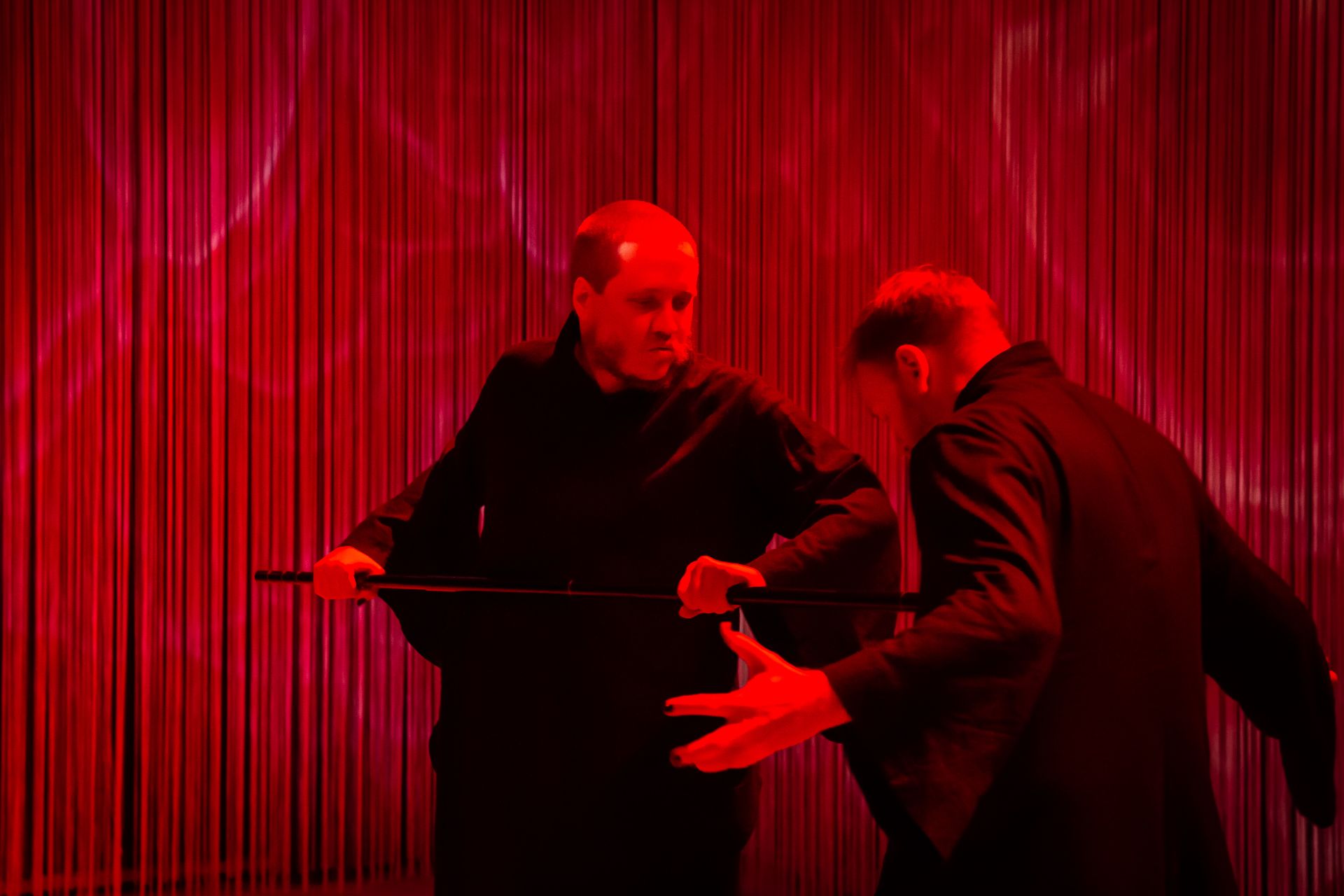 Dramaattisen punaisessa valaistuksessa DuvTeaternin tanssija Emil tökkää tanssikepillä tanssija-Eeroa torsoon. Molemmilla on päällään mustat kimonot.